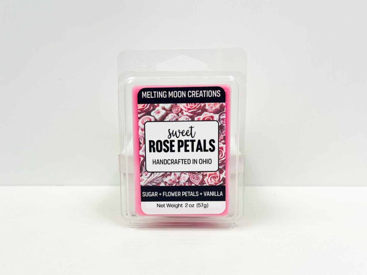 A clear plastic package with a pink label that reads 'Sweet Rose Petals' from Melting Moon Creations. The label includes the scent listed as Sugar + Flower Petals + Vanilla and it states the net weight of the product is 2 oz (57g).