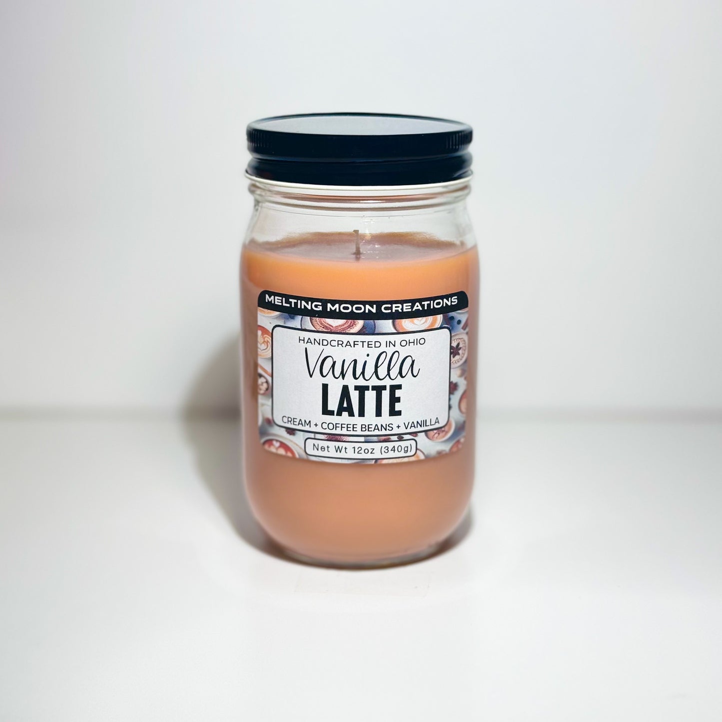 Vanilla Latte candle in glass jar with black twist on lid sitting on a white background. Candle wax is tan. Label designed by Melting Moon Creations.