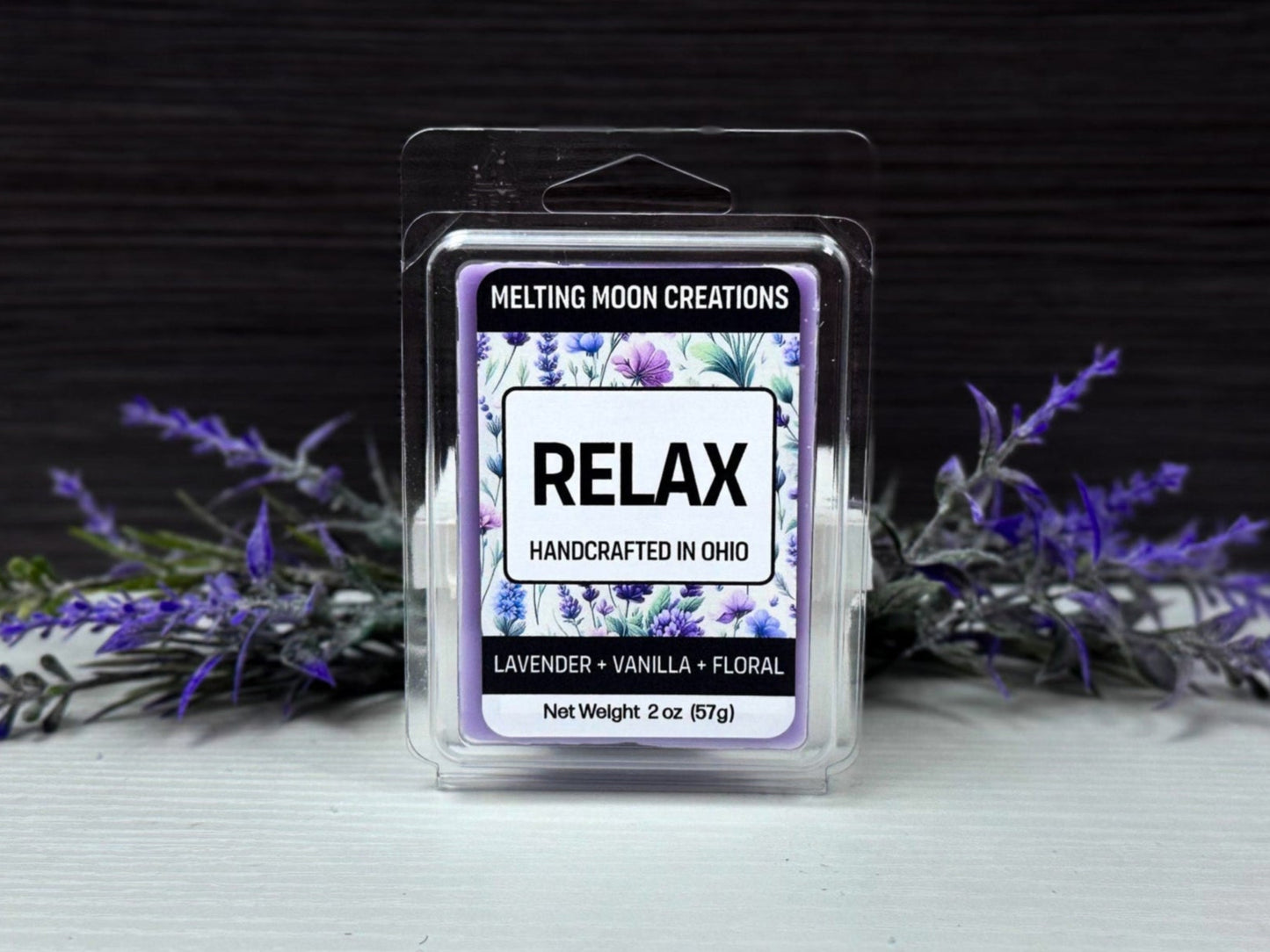 Relax wax melt sitting on white tabletop with lavender flowers positioned behind. Dark gray background. Labeled by Melting Moon Creations.