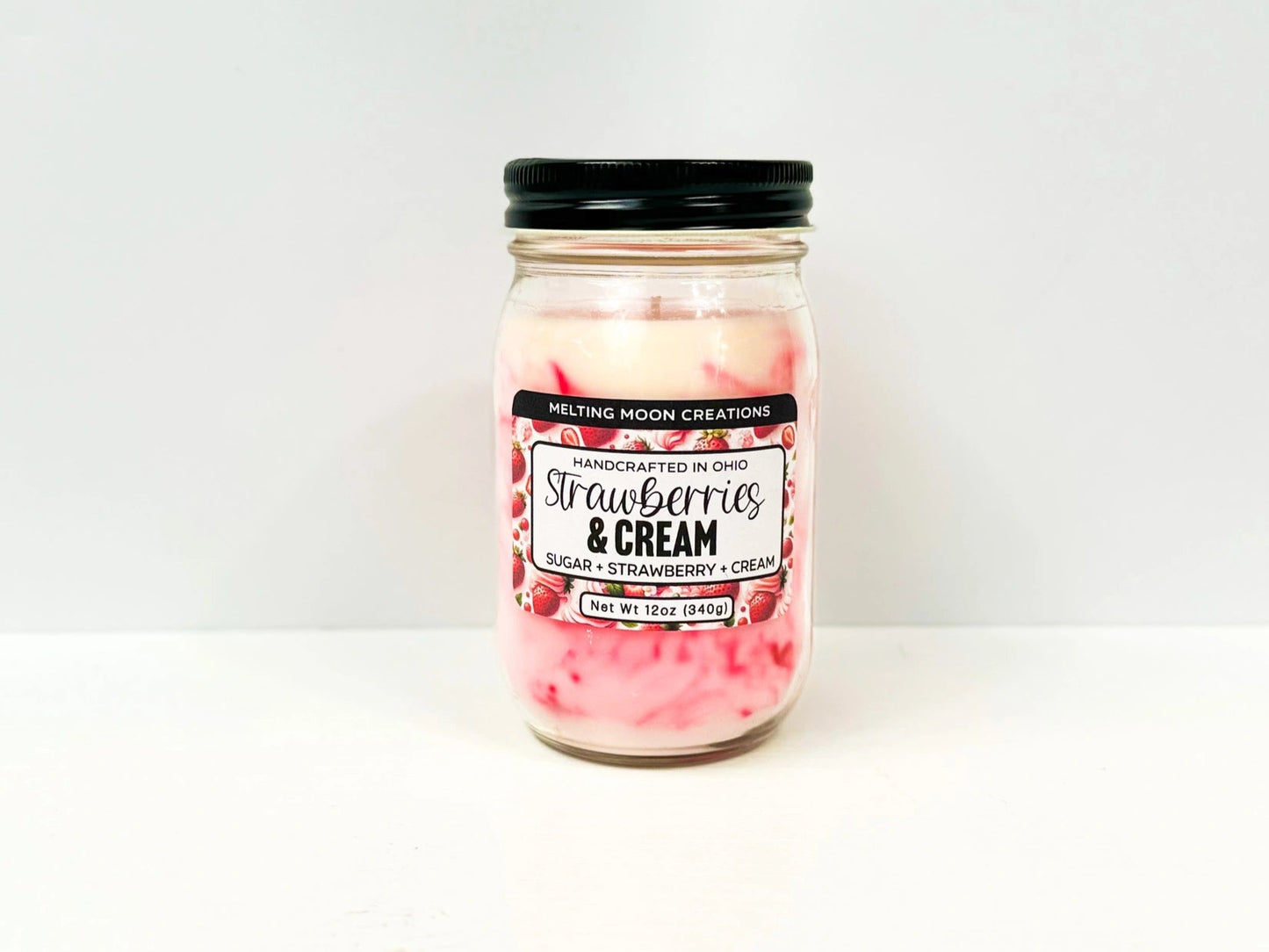 Strawberries and Cream candle in glass jar with back twist on lid sitting on white backdrop. Pink and white marbled wax. Label created by Melting Moon.