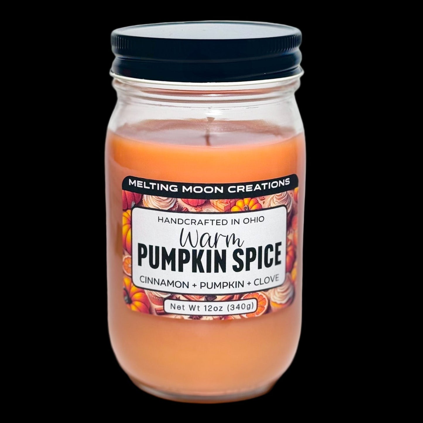 Warm pumpkin spice dyed candle in a glass jar with black screw on lid sitting on a white backdrop. Label designed by Melting Moon Creations.