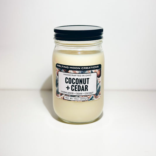 Coconut + Cedar candle in glass jar with black twist on lid sitting on white backdrop. Candle label designed by Melting Moon Creations.