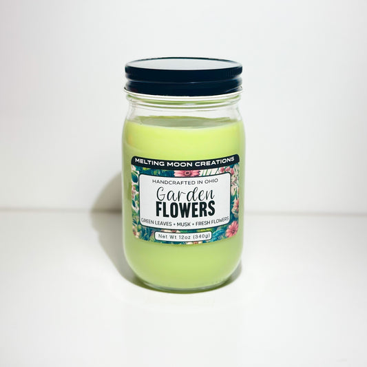 Garden Flowers candle in glass jar with black twist on lid. Sitting on white backdrop. Label designed by Melting Moon Creations.