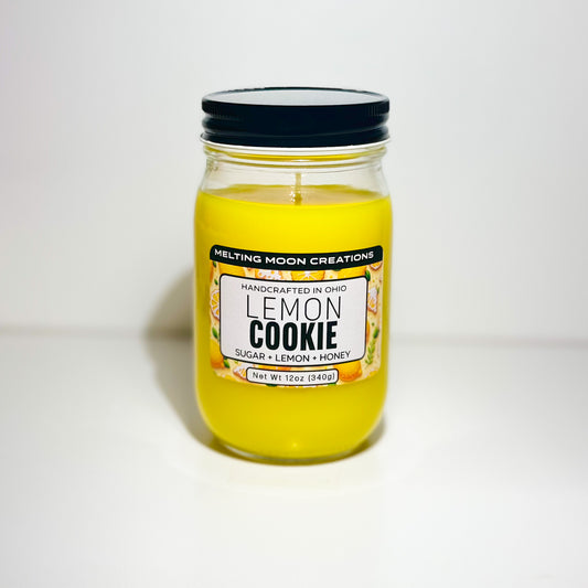 Lemon Cookie candle in glass jar with black twist on lid sitting on white backdrop. Candle wax is yellow. Label designed by Melting Moon Creations.