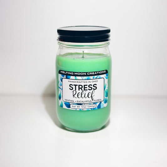 Stress Relief candle in glass jar with black screw on lid sitting on white backdrop. Green candle wax. Candle label designed by Melting Moon Creations.