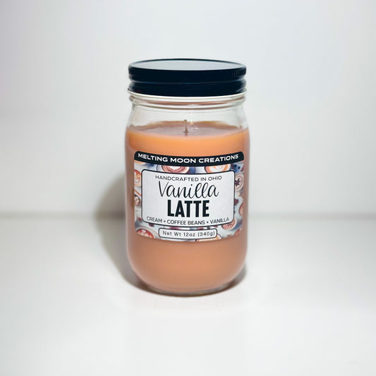 Vanilla Latte candle in glass jar with black twist on lid sitting on a white background. Candle wax is tan. Label designed by Melting Moon Creations.