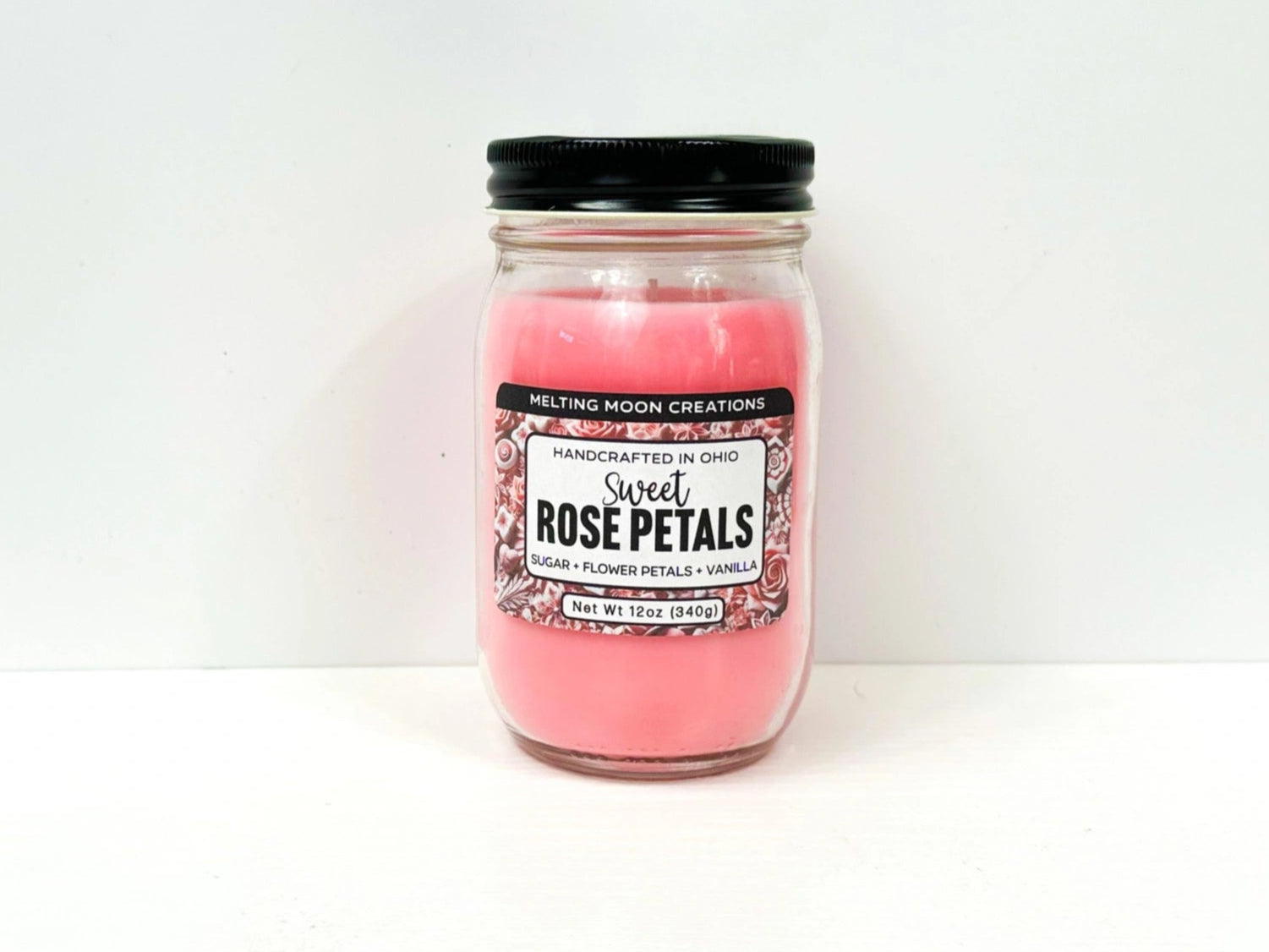 Sweet Rose Petals candle in glass jar with black twist on lid on white background. Pink candle wax. Candle label designed by Melting Moon.